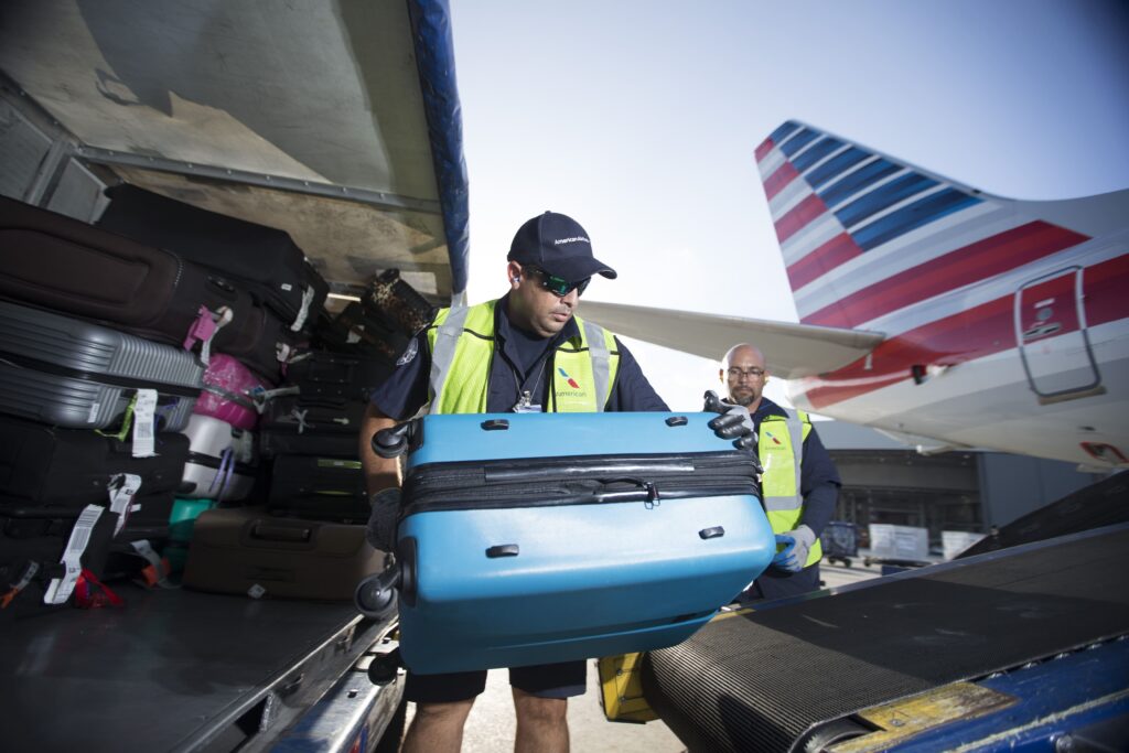 Ground crew loading a checked bag into an American Airlines aircraft